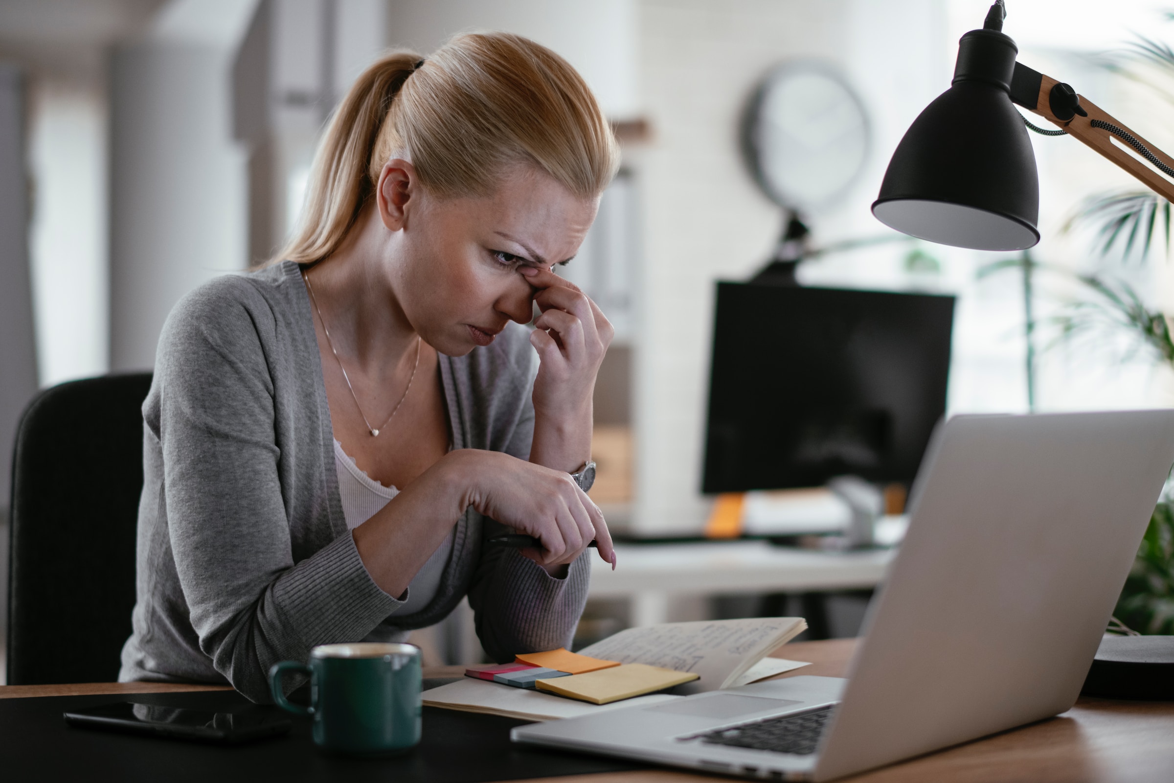 Woman bent over her desk with her laptop and papers.